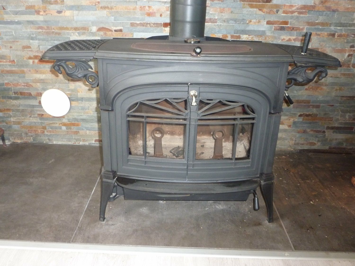 Poêle à bois en fonte noire contre un mur en briques. Une cheminée s'élève du poêle.