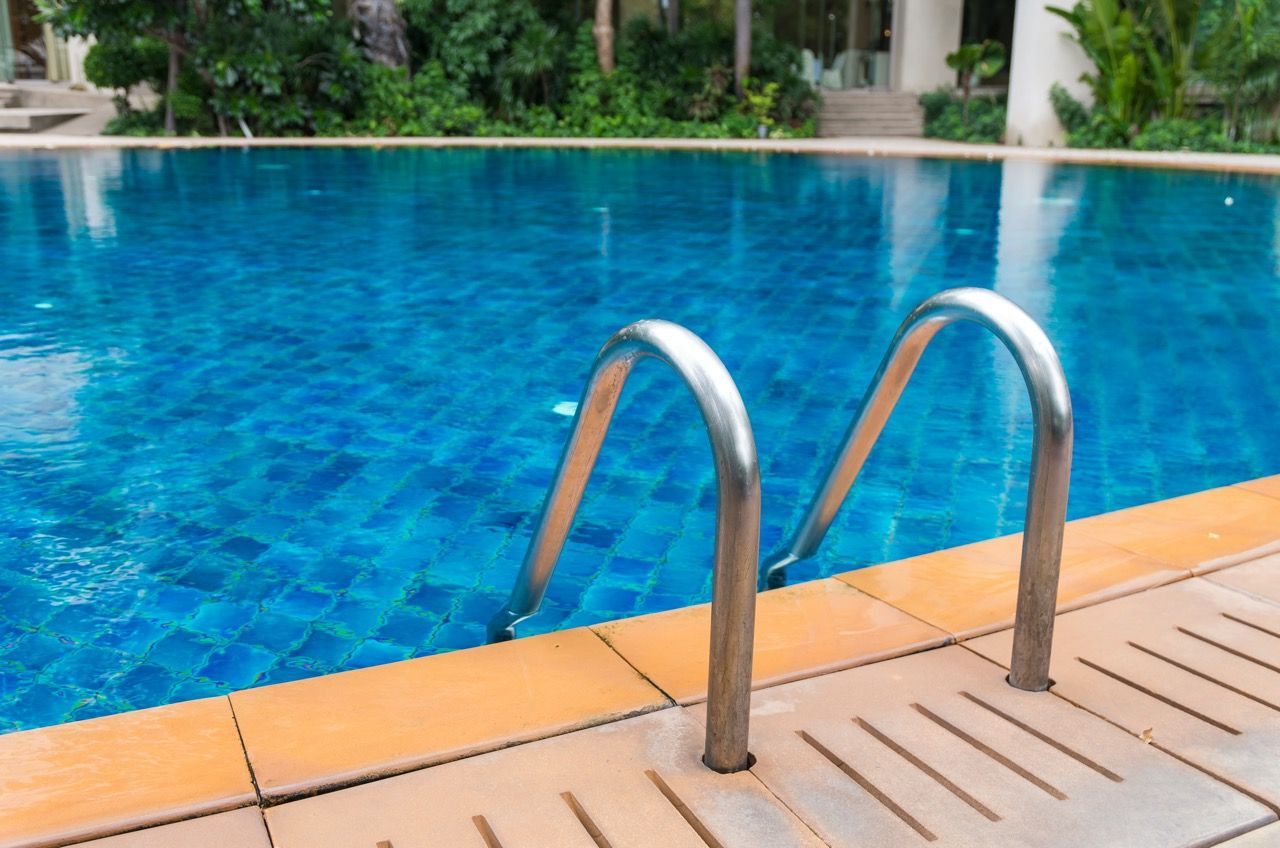 Escalera metálica que conduce a una piscina revestida de azulejos de color azul brillante con una terraza.