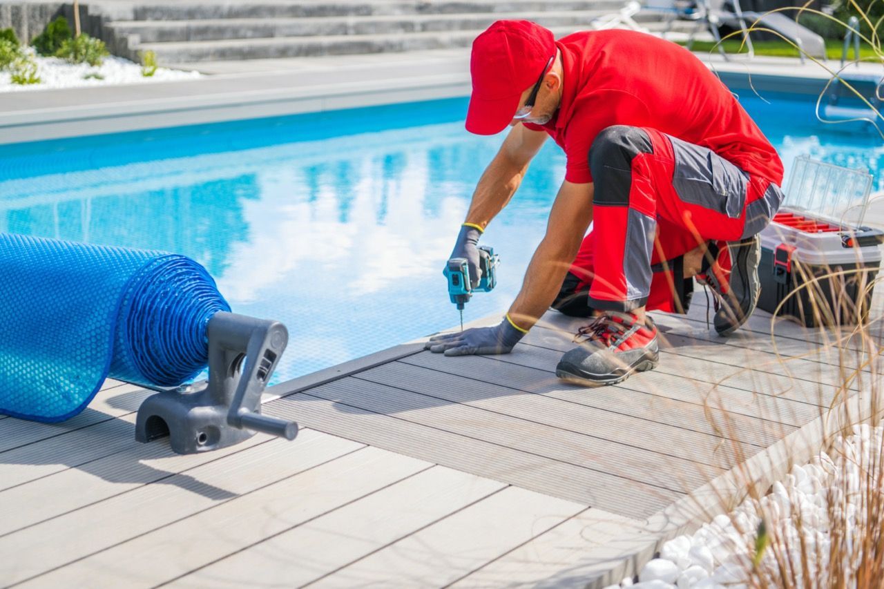 Una persona con uniforme rojo arrodillada junto al borde de una piscina para reparar el revestimiento cerc.