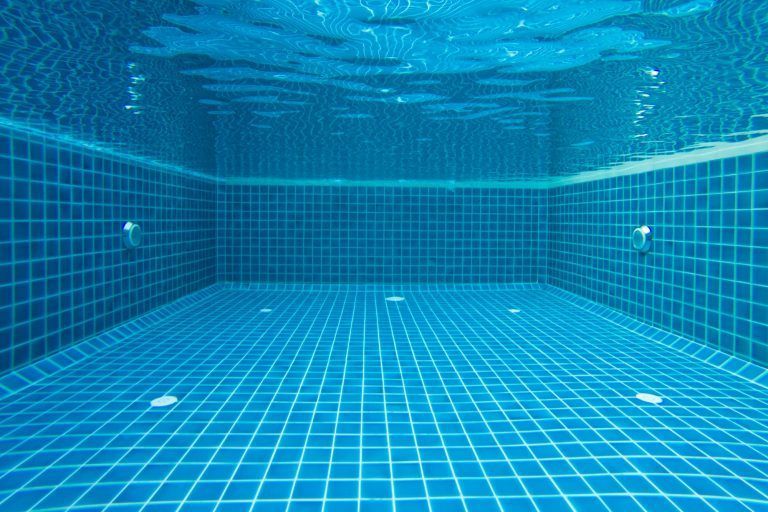 Vista subacuática de una piscina rectangular con paredes y suelo de azulejos azules y agua ondulante en la superficie.