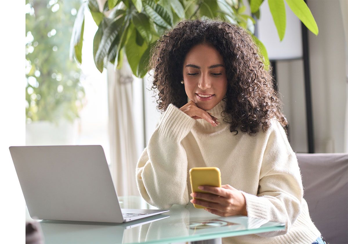 Femme devant son ordinateur qui tient son portable