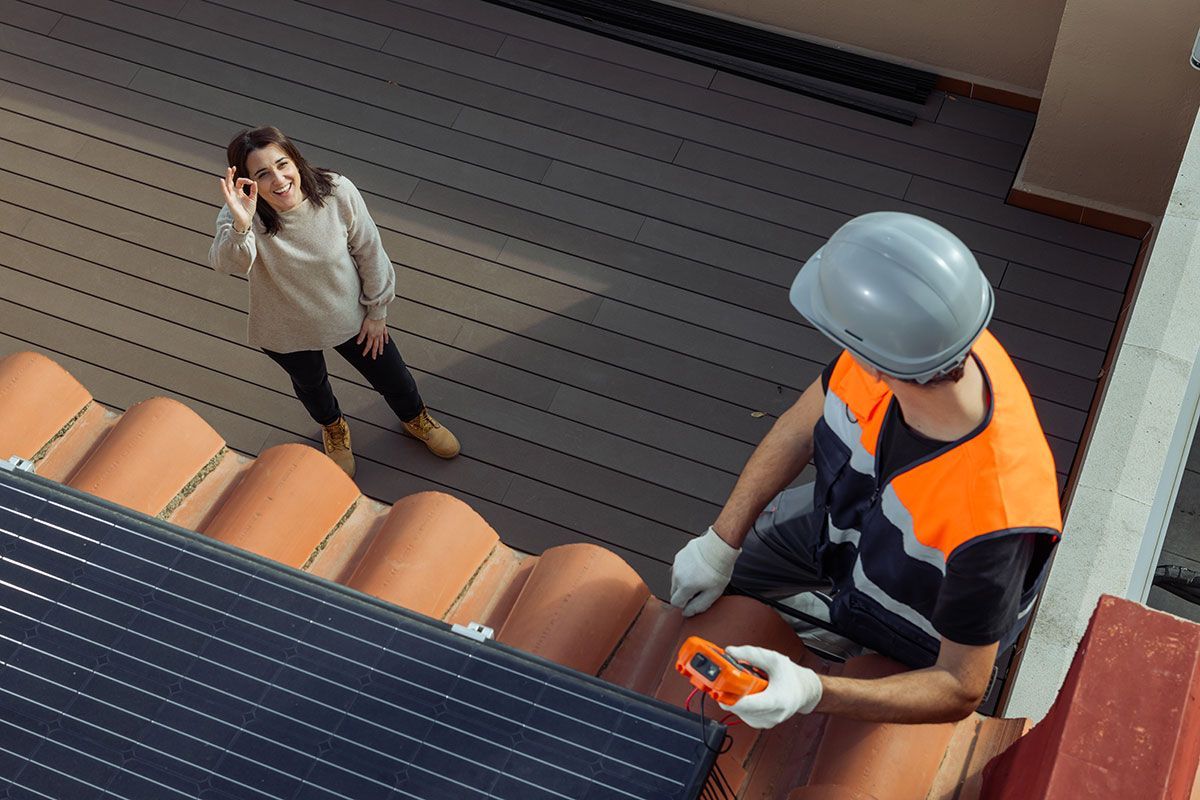 Femme qui fait signe que c'est bien à un ouvrier qui pose des panneaux solaires