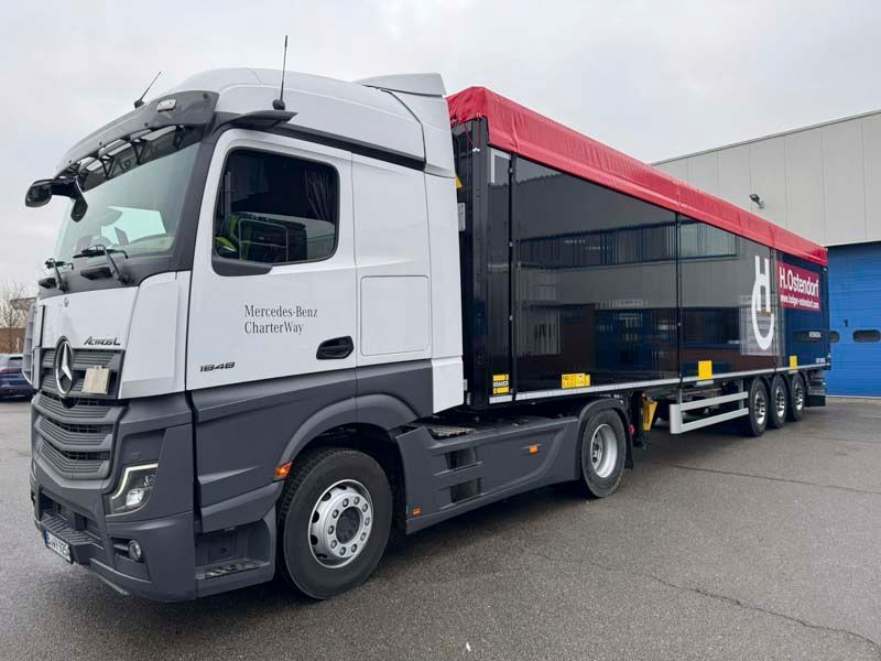 Mercedes-Benz-Sattelzug mit schwarz-rotem Anhänger, im Freien geparkt.