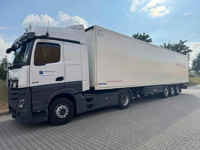 Weißer Sattelschlepper mit langem Anhänger, geparkt auf dem Bürgersteig unter blauem Himmel. Der LKW hat dunkelgraue Akzente.