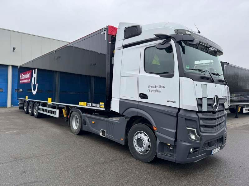 Mercedes-Benz Sattelschlepper mit Pritschenanhänger, weiß und dunkelgrau, vor einem Gebäude geparkt.