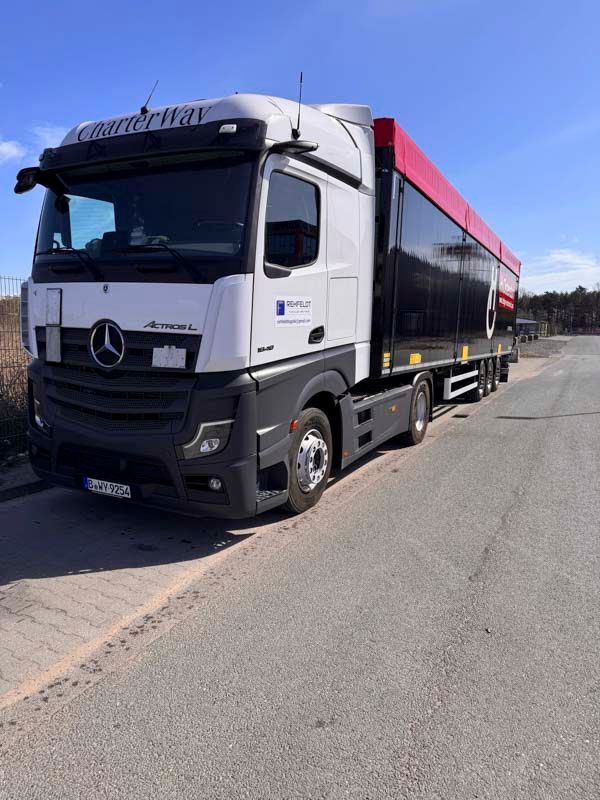 Weiß-schwarzer Sattelschlepper mit einem roten Container auf Asphaltstraße geparkt. Blauer Himmel im Hintergrund.