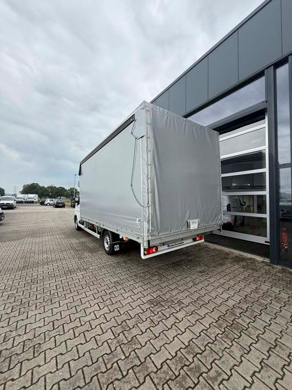 Lastwagen mit grauer Plane, der an einem bewölkten Tag vor einem modernen Gebäude geparkt ist.