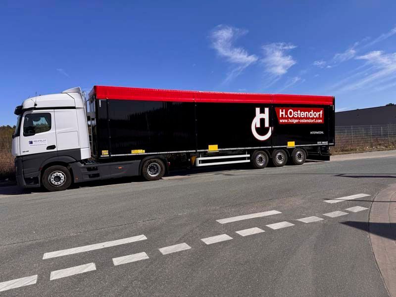 Schwarz-roter LKW von H. Ostendorf auf Asphaltstraße mit weißen Linien geparkt; blauer Himmel im Hintergrund.
