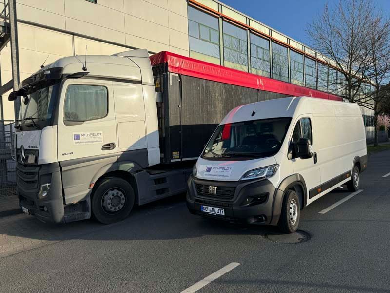 Ein weißer Sattelschlepper und ein weißer Lieferwagen parken auf einer Straße neben einem Gebäude.