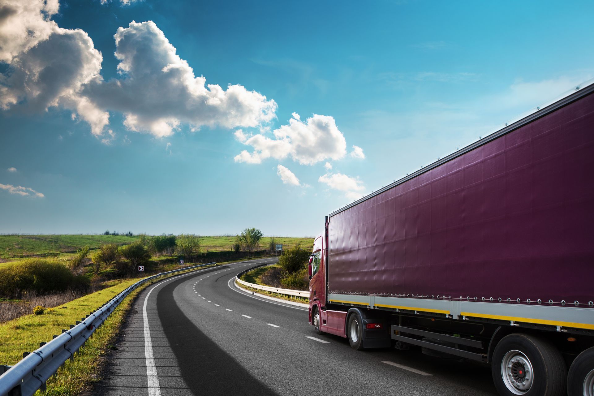 Weißer Sattelschlepper fährt auf einer Autobahn mit heller Sonne am Himmel und grasbewachsenem Mittelstreifen.