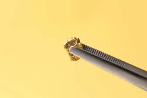 Pinzas que sostienen un pequeño anillo de oro sobre un fondo amarillo.