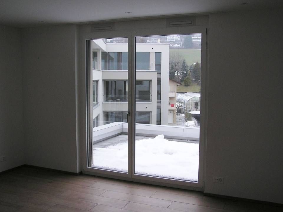 Ein leerer Raum mit einer Glasschiebetür, die zu einem Balkon führt. Foto von der Adolf Nussbaumer Fensterbau AG