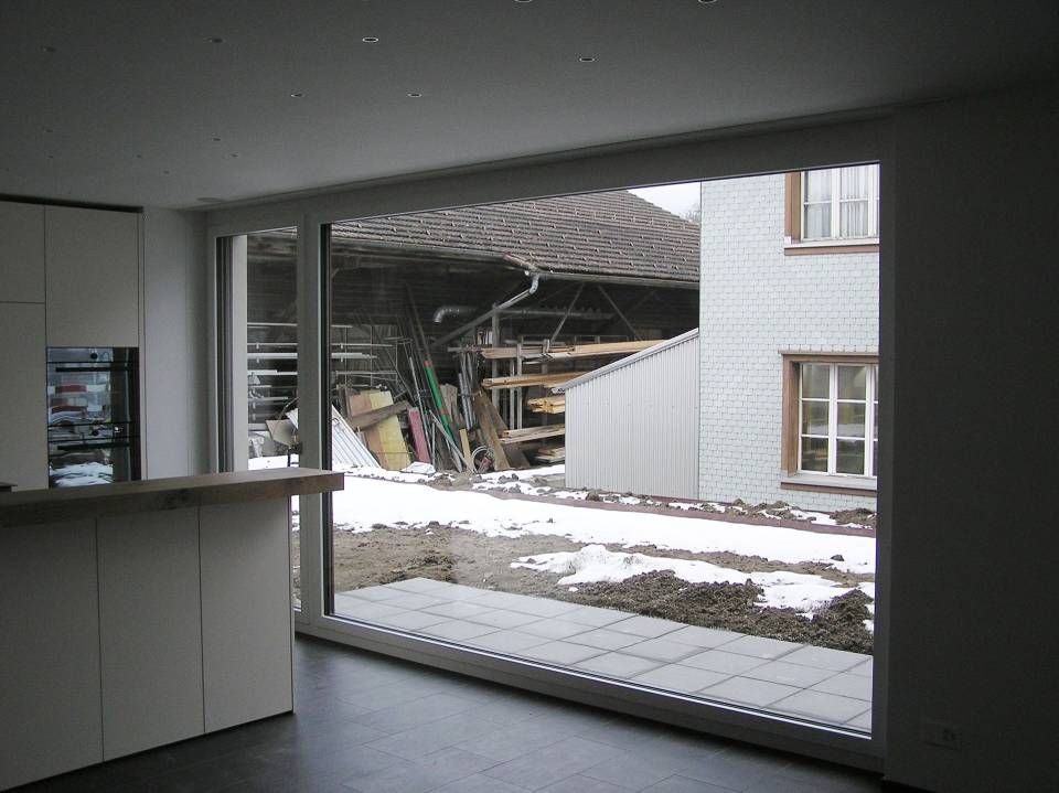 Eine Küche mit einer Glasschiebetür mit Blick auf einen verschneiten Hof. Foto von der Adolf Nussbaumer Fensterbau AG
