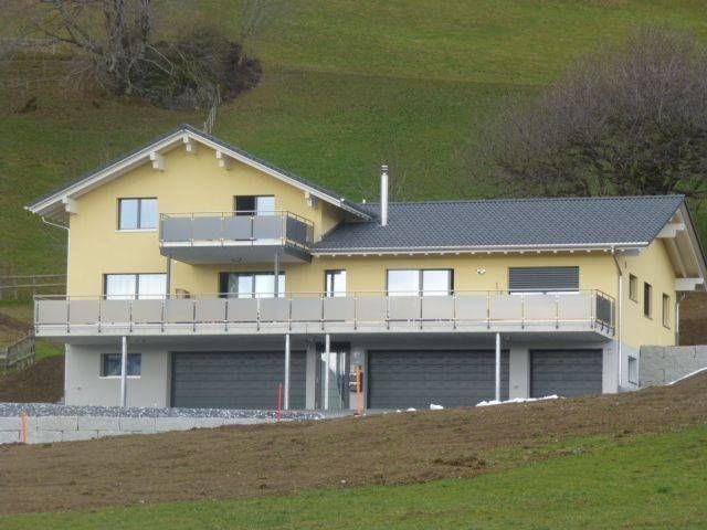 Ein gelbes Haus mit einem schwarzen Dach steht auf einem Hügel. Foto von der Adolf Nussbaumer Fensterbau AG