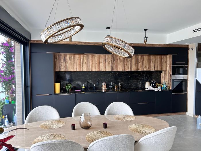 Cocina y comedor modernos de planta abierta con armarios negros, detalles en madera y lámparas colgantes.