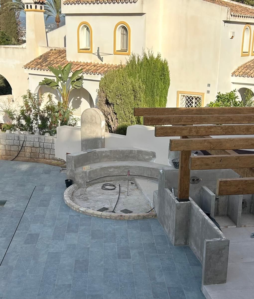 Patio con fogata de piedra integrada, bancos de madera y una casa de estuco color crema al fondo.