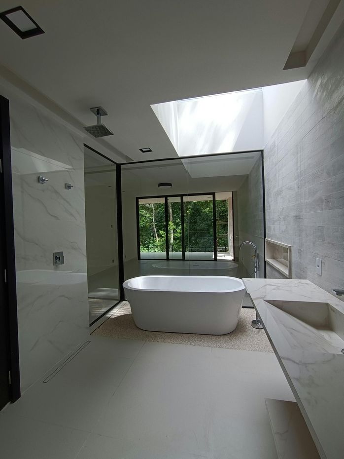 Baño moderno con bañera exenta, ventanal grande, paredes de piedra blanca y lavabo suspendido.