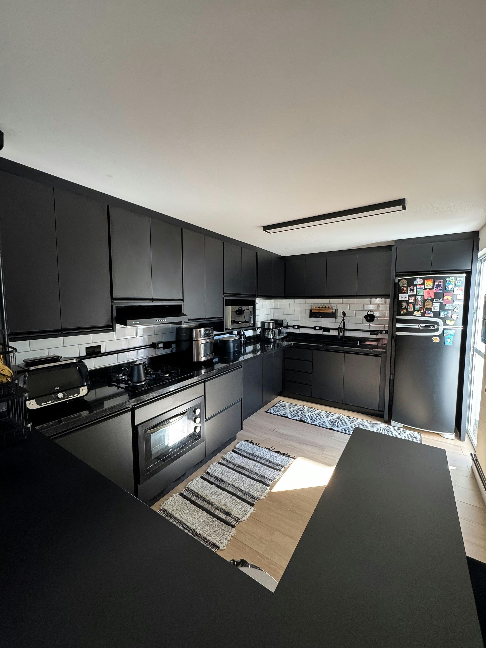 Cocina moderna negra con electrodomésticos de acero inoxidable, salpicadero de azulejos y una alfombra estampada en el suelo.