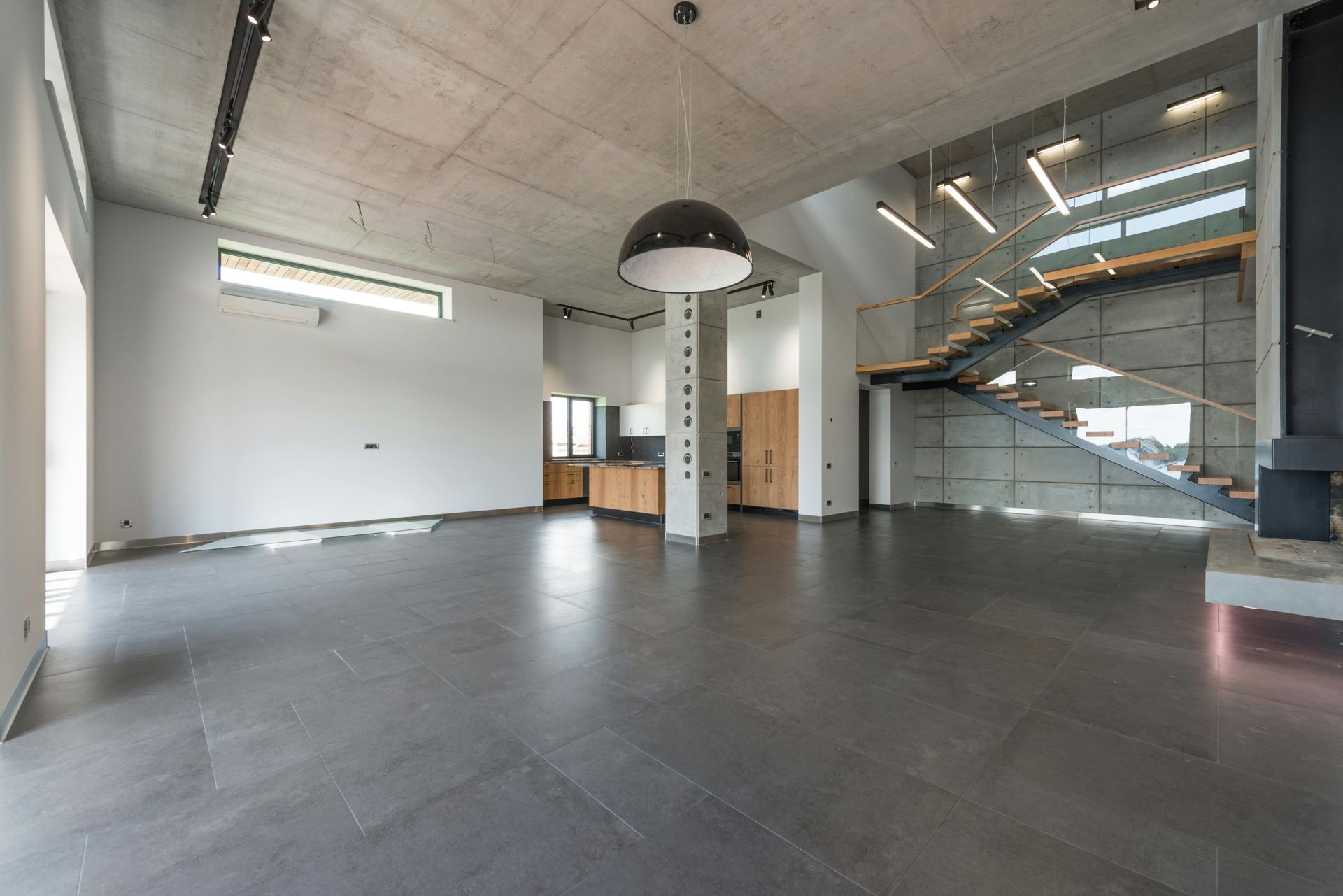 Interior de un loft moderno y vacío con suelos de hormigón, techo a la vista y escalera de cristal.