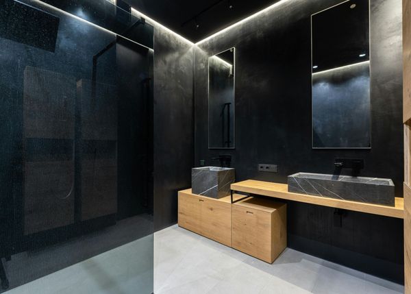 Baño moderno de color negro con tocador de madera, espejo grande y ducha acristalada.