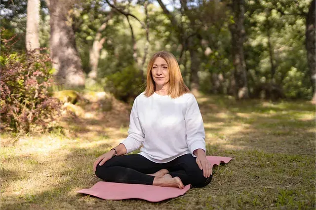 Una mujer está sentada en una esterilla de yoga en un parque.