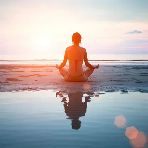 Una mujer está sentada en posición de loto en la playa al atardecer.