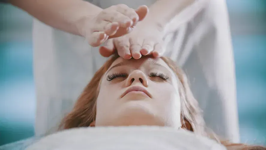 Una mujer está recibiendo un tratamiento de reiki en la frente.