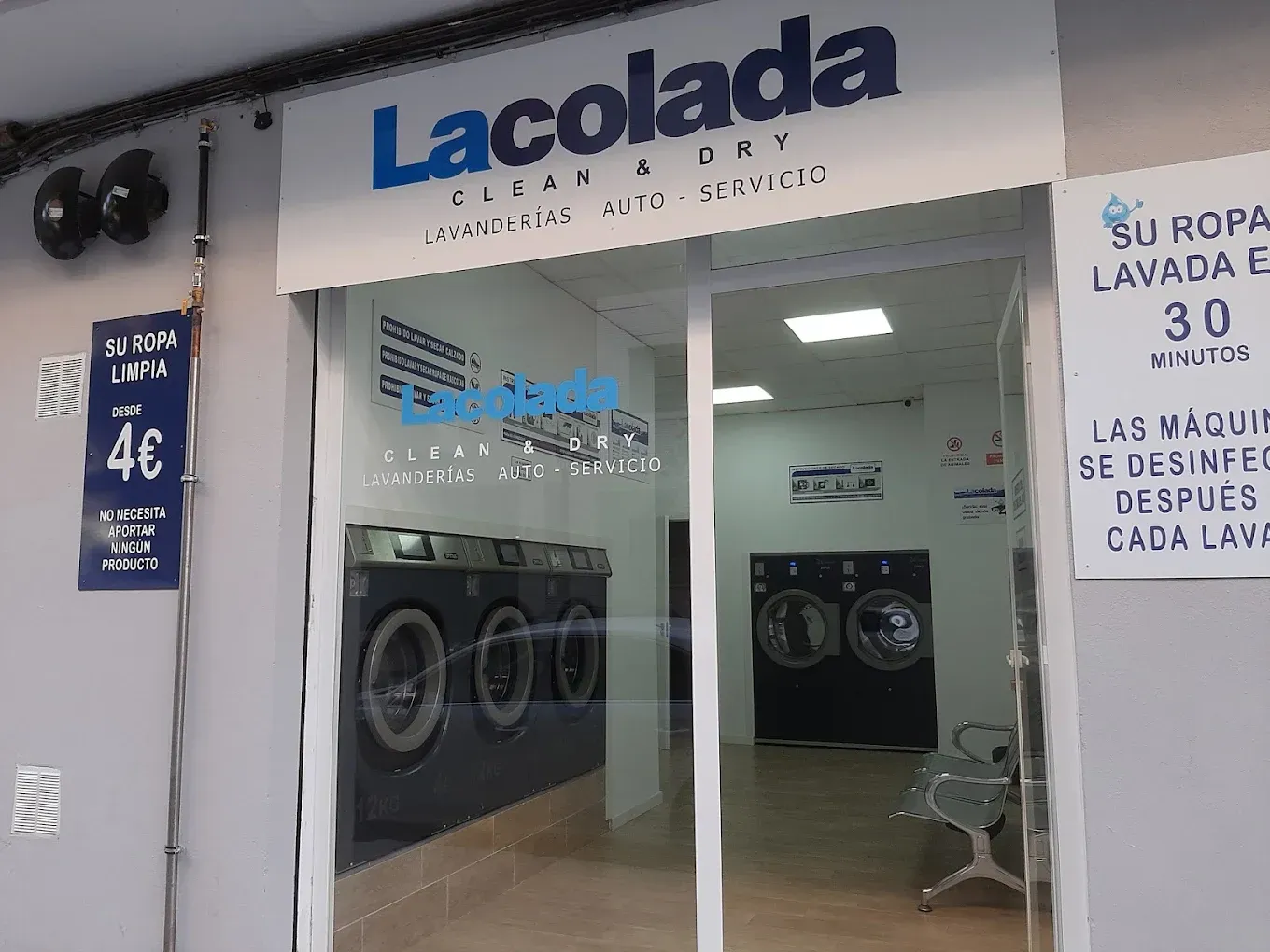 Lavandería con escaparate de puertas de cristal, imágenes de lavadoras y un letrero azul de «LaColada».