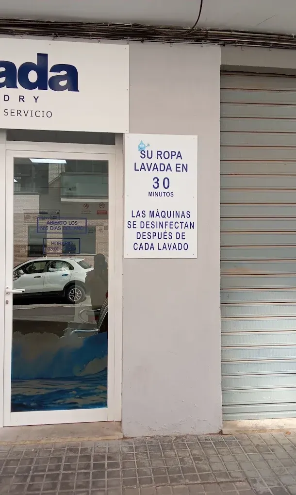 Entrada de un local con un letrero blanco en español y una puerta de cristal que refleja un coche aparcado.