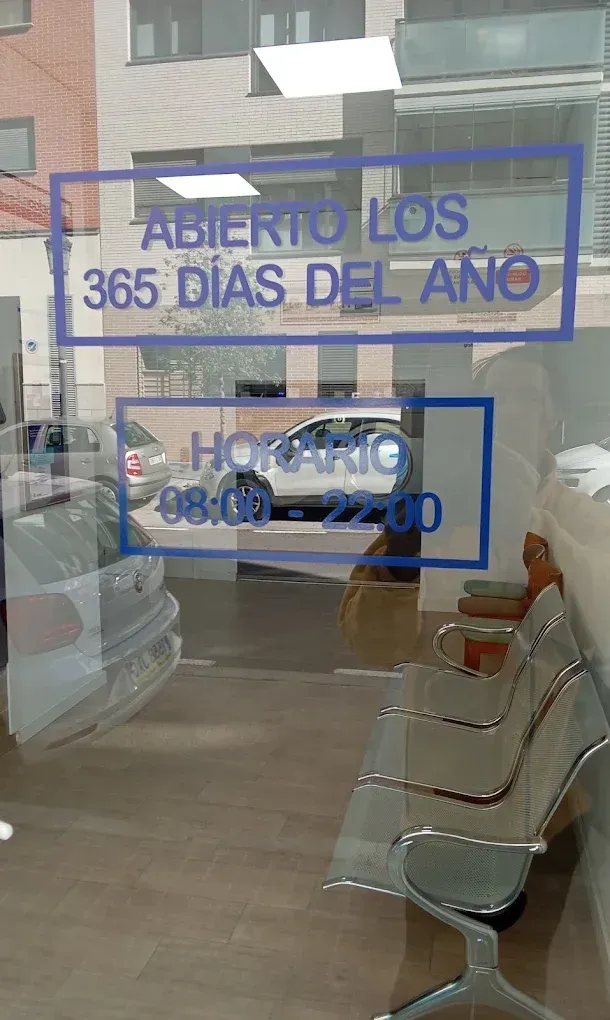 Letrero en el escaparate que dice «ABIERTO LOS 365 DÍAS DEL AÑO» y muestra el horario; se ven sillas en el interior.