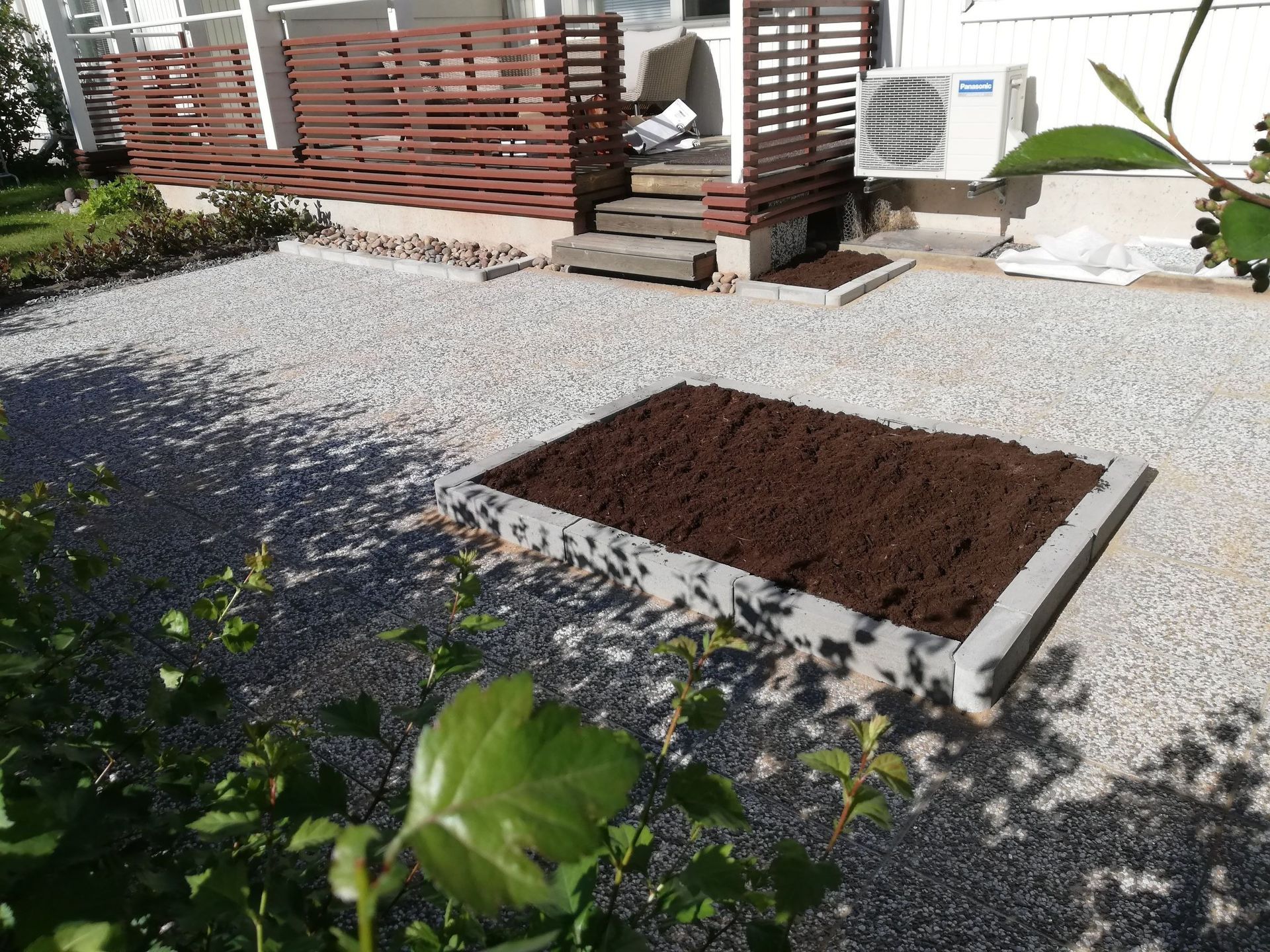 Tuoreesti muokattu puutarhapenkki soraterassin ja puisen aidan vieressä aurinkoisella takapihalla