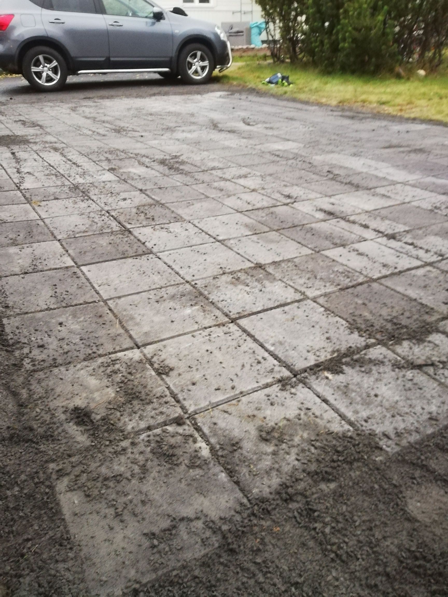 Märkä päällystetty ajotie, jonka vasempaan yläkulmaan on pysäköity harmaa katumaasturi.