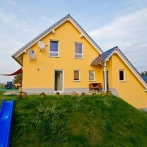 Gelbes Einfamilienhaus mit Satellitenschüsseln am Giebel.