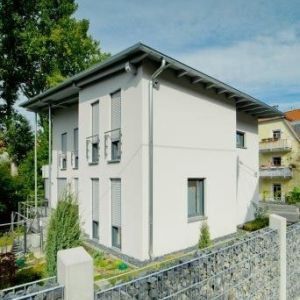 Eckansicht eines Hauses mit grauer Putzfassade und französischen Balkonen.