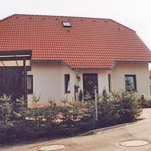 Breitformatige Ansicht eines flachen Wohnhauses mit großem roten Ziegeldach und einem kleinen quadratischen Dachfenster.