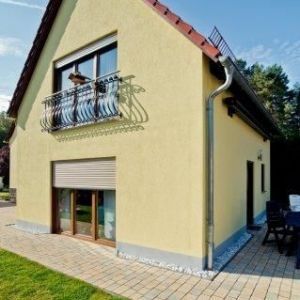 Hellgelbes Haus mit Ziegeldach und Balkon mit dekorativem Metallgitter.