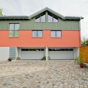 Frontansicht eines Giebels mit vertikaler, grüner Holzlattung und drei Fenstern.