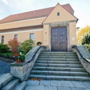 Hoher, schlichter Kirchturm mit kleinen Fensteröffnungen vor herbstlichen Bäumen und blauem Himmel.