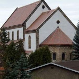 Massives, dunkles Holzportal einer Kirche mit Steingewand und kleiner Treppe im Eingangsbereich.