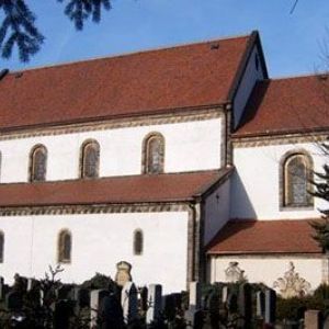 Helle Außenwand einer Kirche mit drei Rundbogenfenstern unter einem roten Ziegeldach.