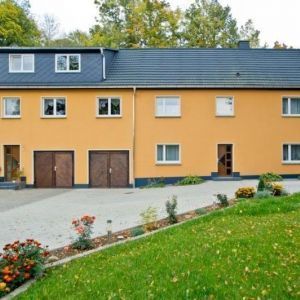 Weißes Gebäude mit markantem Krüppelwalmdach und Gaubenband.