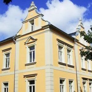 Detail eines prunkvollen gelben Hauses mit einem geschwungenen Volutengiebel und weißen Stuckverzierungen an den Fenstern.