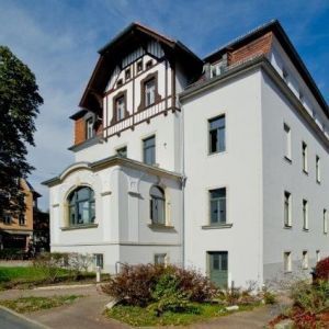 Ein elegantes weißes Eckhaus mit dunklem Zierfachwerk im Dachgeschoss und einem kleinen Erker.