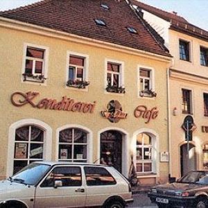 Außenansicht einer Konditorei und eines Cafés in einem gelben Altbau mit dekorativen Fensterrahmen und Blumenkästen.