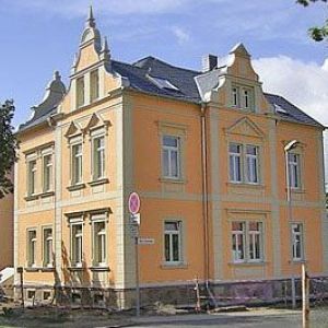 Eine gelbe, historische Stadtvilla mit zwei markanten Ziergiebeln und einem grauen Schieferdach.