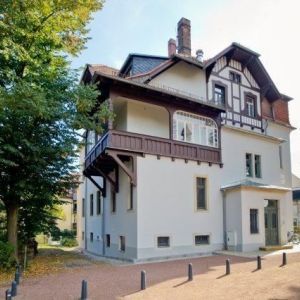 Historisches Gebäude mit dunklem Holzbalkon und Krüppelwalmdach.