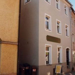 Schlichte, grau-beige Fassade eines sanierten Stadthauses mit weißen Fensterumrandungen und einer leeren Werbefläche.