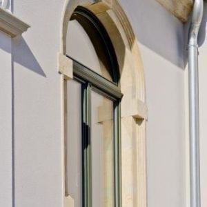 Detailaufnahme eines eleganten, dunkel gerahmten Bogenfensters, das tief in die helle Fassade eingelassen ist.