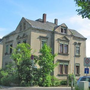 Perspektivische Ansicht eines grauen, leerstehenden Wohngebäudes mit Mansarddach und historischen Gauben.