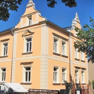 Prachtvolle, frisch sanierte Altbaufassade in Gelb und Weiß mit dekorativen Giebeln und aufwendigen Fensterumrandungen.